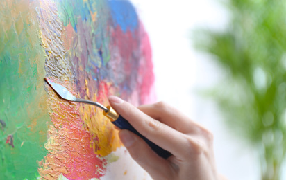 Photo of Artist painting on canvas with spatula, closeup