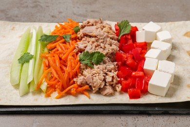 Photo of Delicious tortilla with tuna and vegetables on grey table, closeup. Cooking shawarma