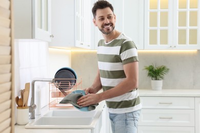 Photo of Man wiping plate with towel above sink in kitchen