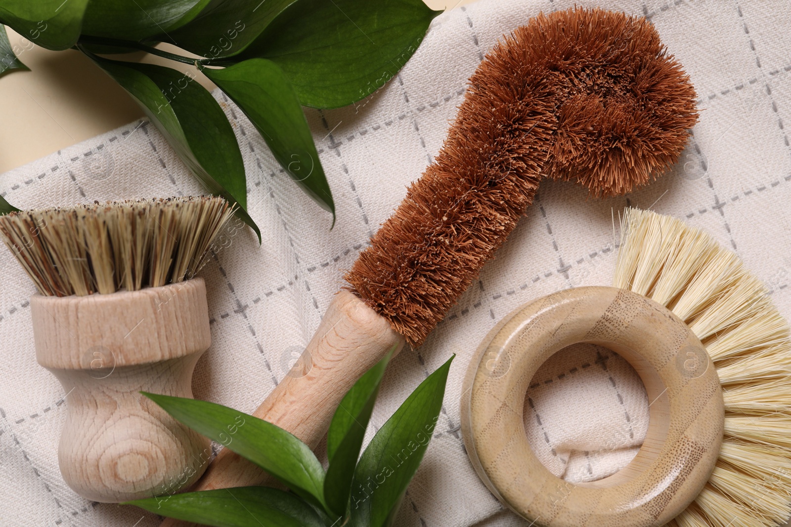 Photo of Cleaning brushes, towel and green leaves on beige background, top view