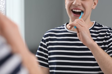 Man brushing his teeth with toothbrush near mirror in bathroom, closeup