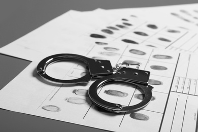 Photo of Police handcuffs and criminal fingerprints card on table, closeup
