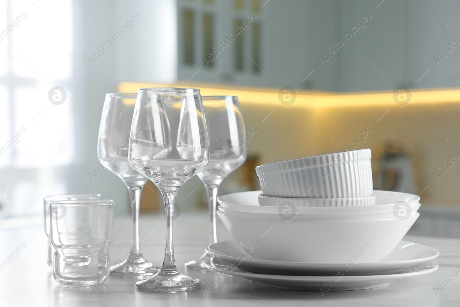 Photo of Different clean dishware and glasses on white marble table in kitchen