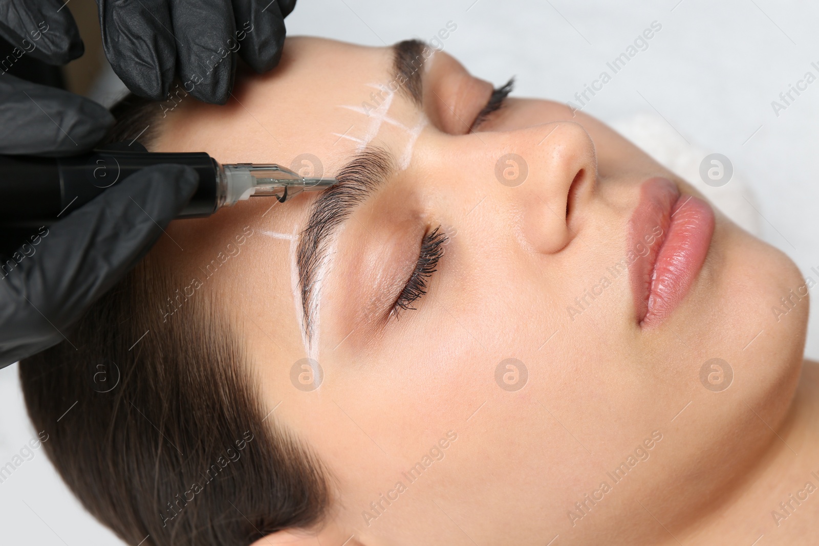 Photo of Beautician making permanent eyebrow makeup to young woman on white background, closeup