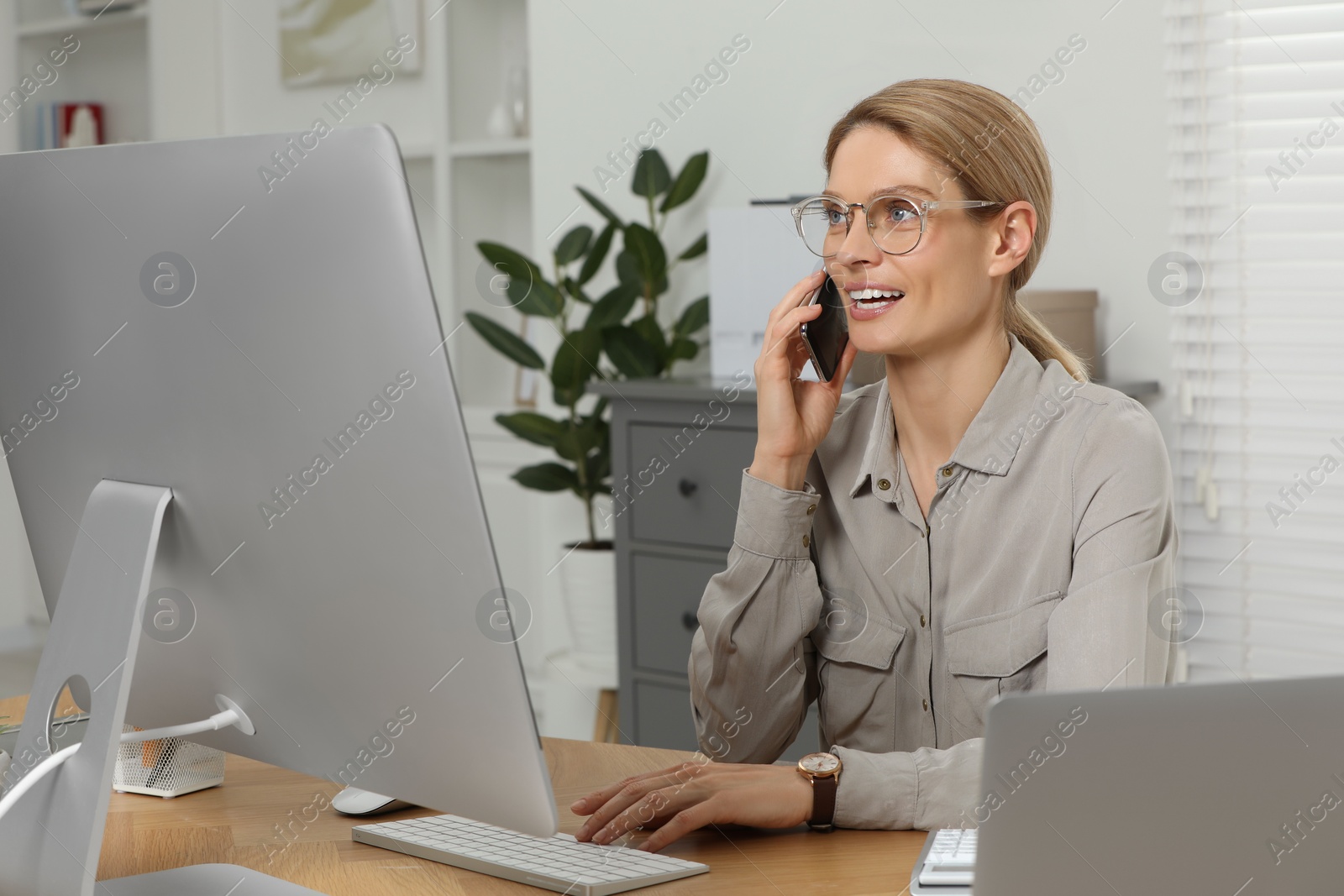 Photo of Professional accountant talking on phone while working at wooden desk in office