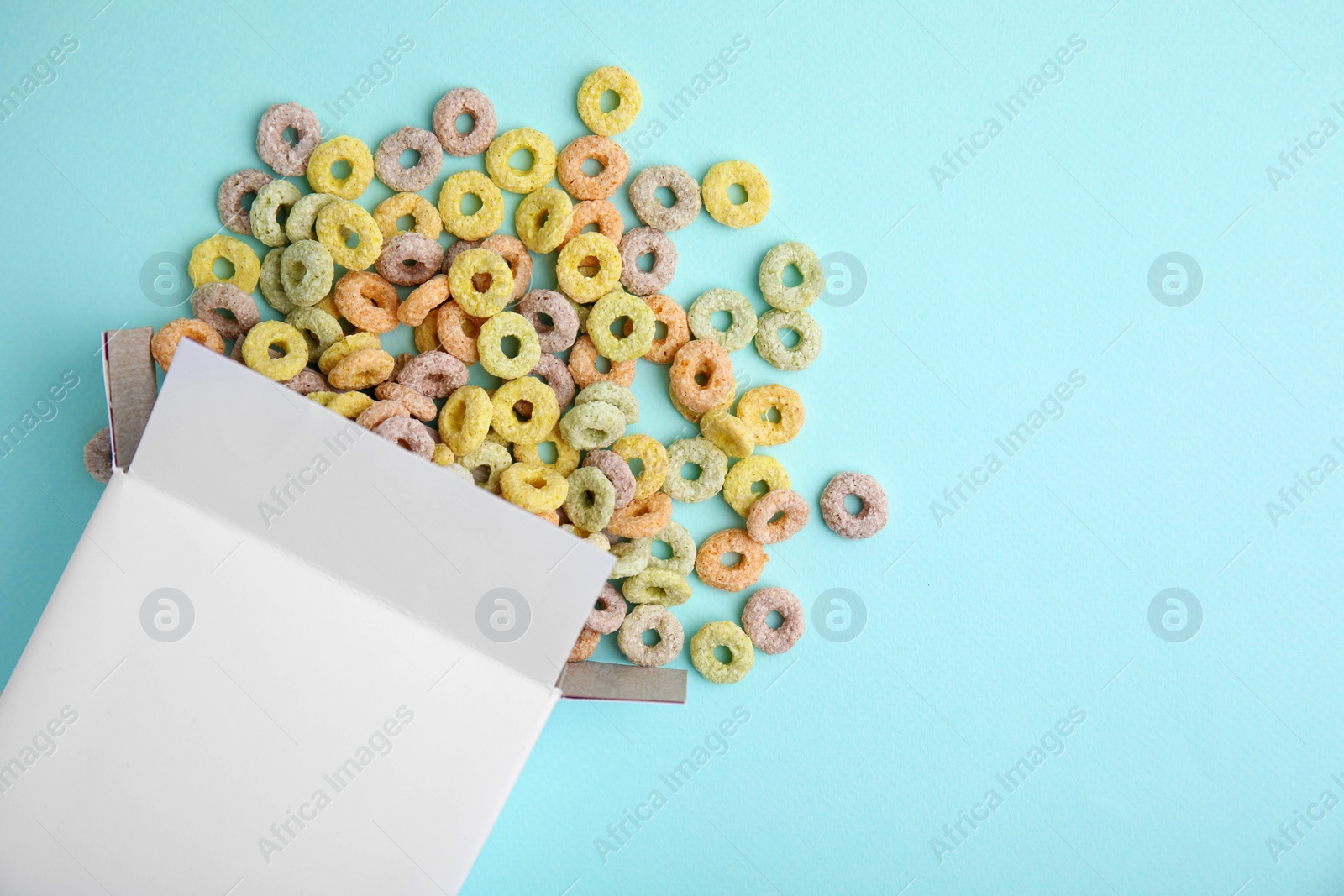 Photo of Paper box with tasty cereal rings on light blue background, flat lay. Space for text