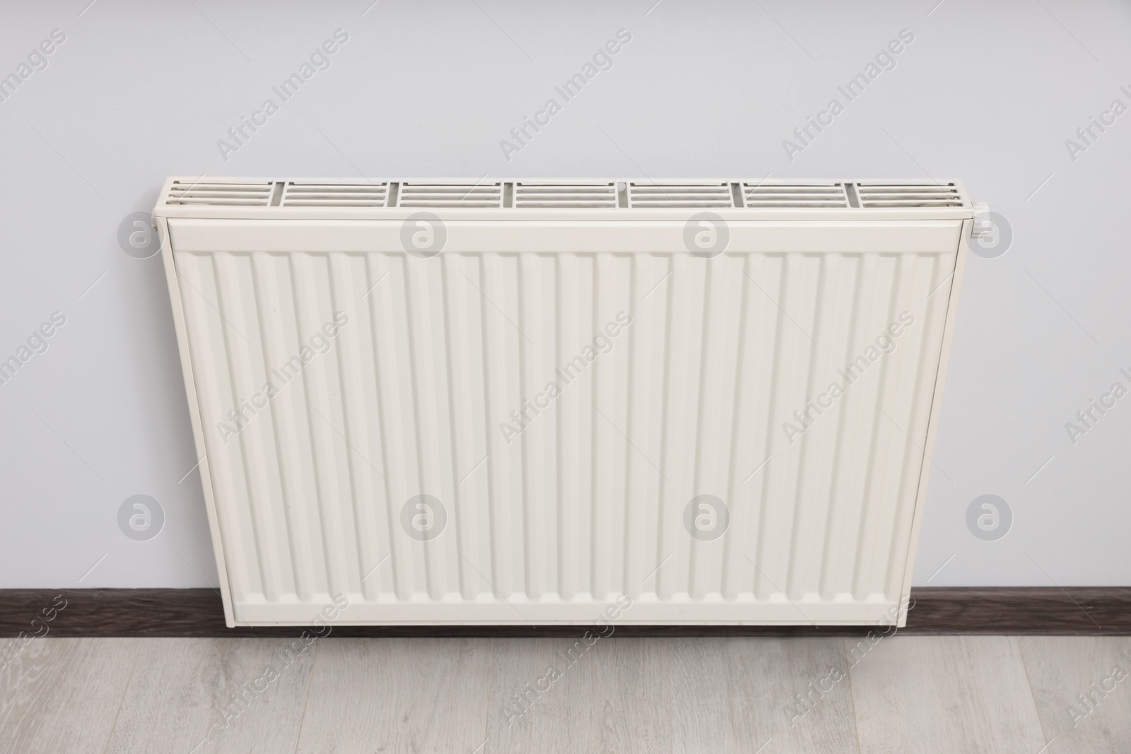 Photo of Modern radiator on white wall in room. Central heating system