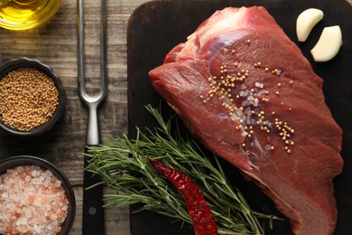 Photo of Piece of raw beef meat, rosemary, spices and fork on wooden table, flat lay