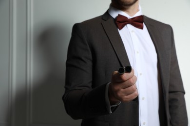 Photo of Man in suit holding stylish cufflinks near white wall, closeup. Space for text