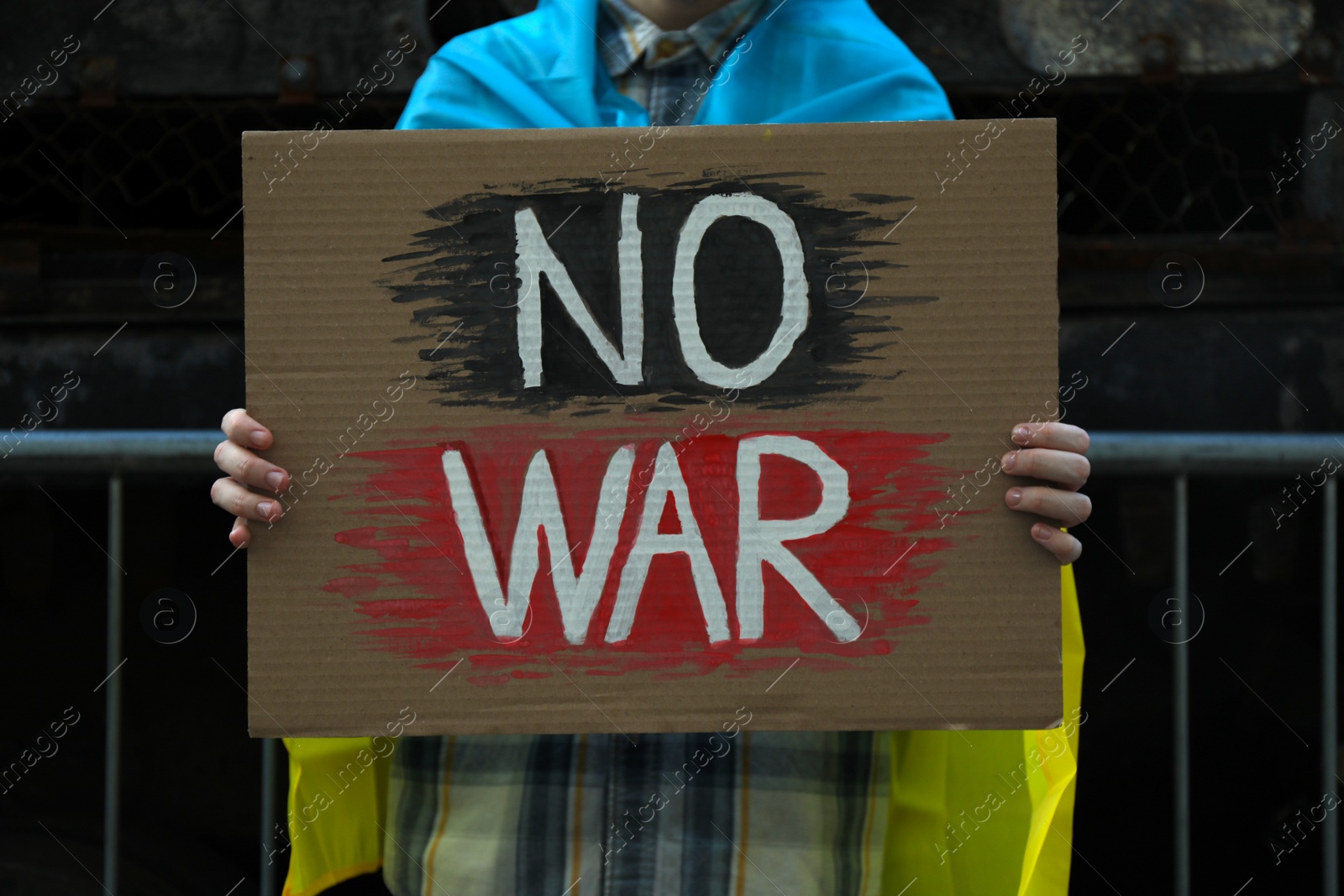 Photo of Woman wrapped in Ukrainian flag holding poster with words No War on street, closeup