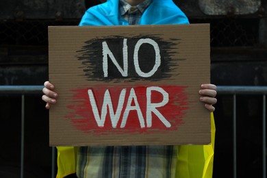 Photo of Woman wrapped in Ukrainian flag holding poster with words No War on street, closeup