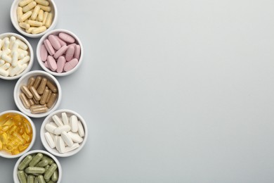 Photo of Different vitamin pills in bowls on grey background, flat lay. Space for text