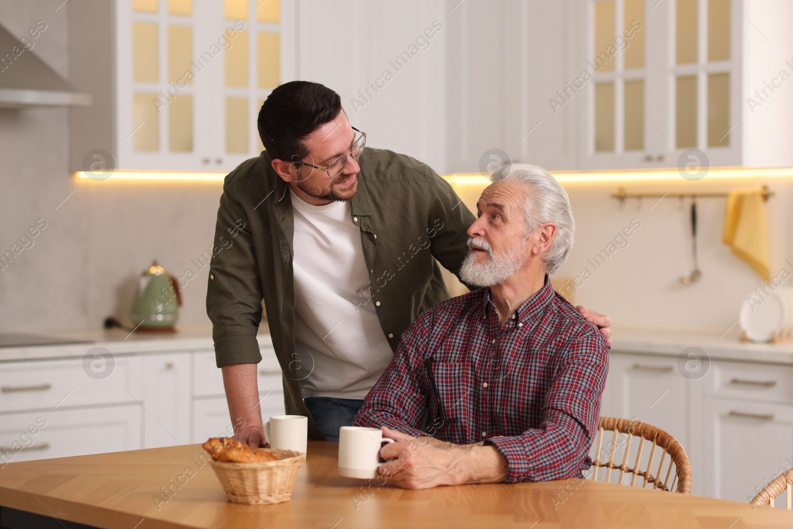 Photo of Happy son and his dad at wooden table in kitchen