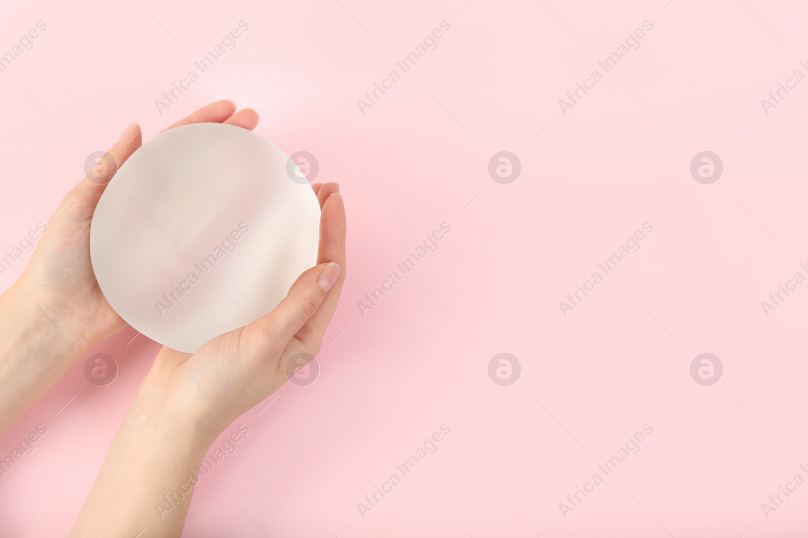 Photo of Woman holding silicone implant for breast augmentation on color background, top view with space for text. Cosmetic surgery