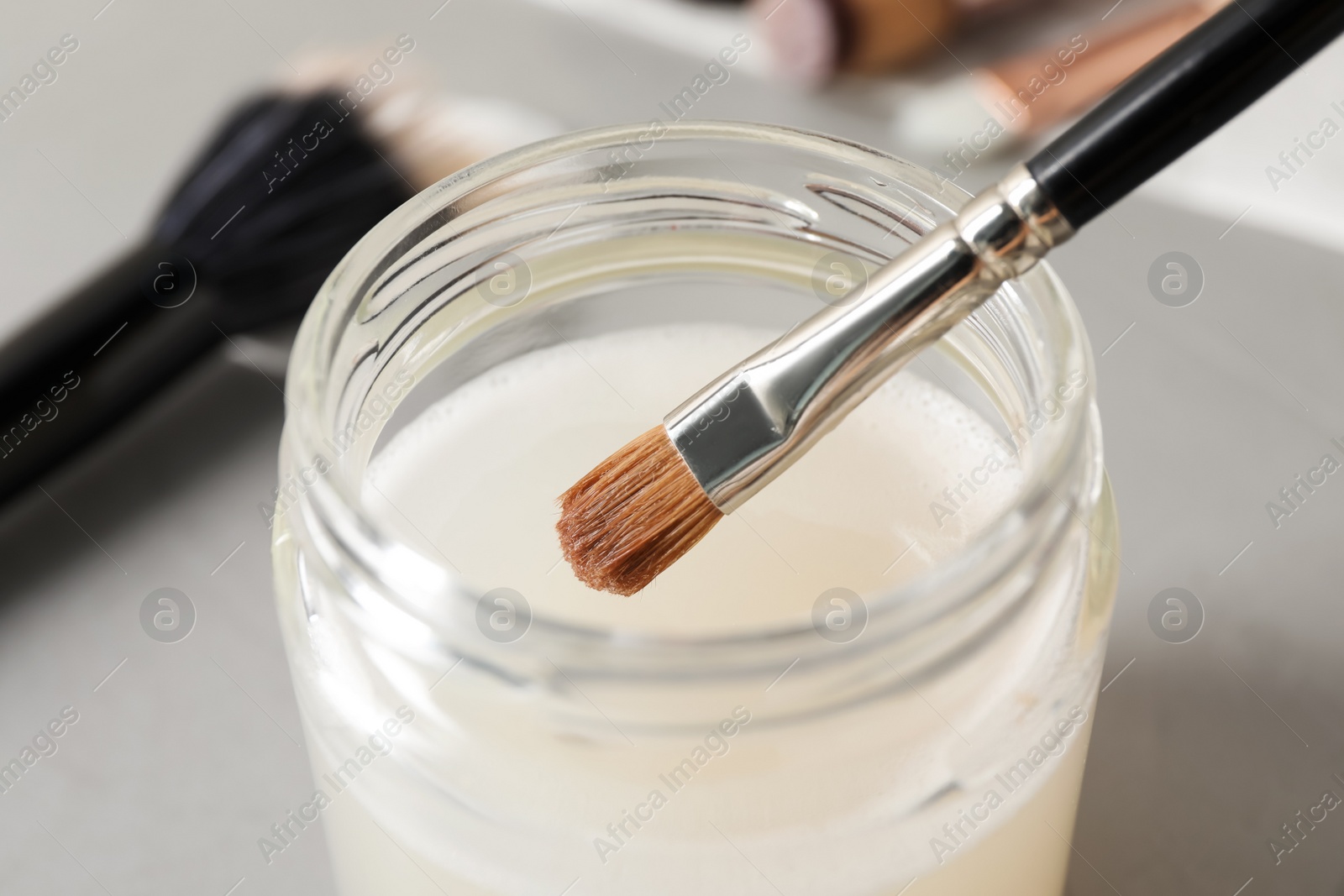 Photo of Cleaning makeup brush in jar with special liquid on grey table, closeup