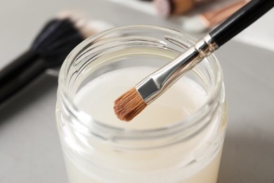 Photo of Cleaning makeup brush in jar with special liquid on grey table, closeup