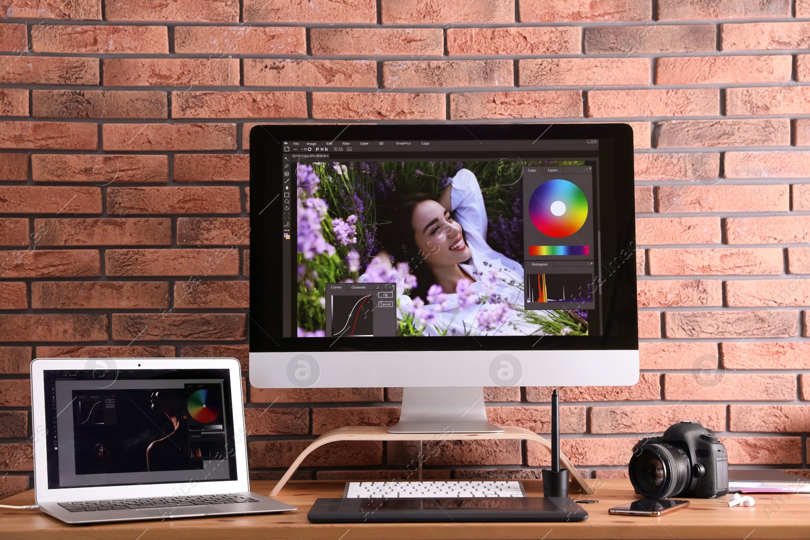 Photo of Modern retoucher's workplace with different digital devices on wooden table near red brick wall