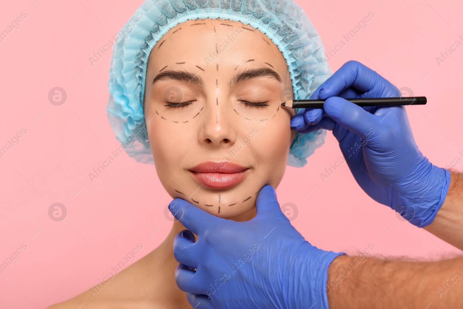 Photo of Doctor with pencil preparing patient for cosmetic surgery operation on pink background, closeup