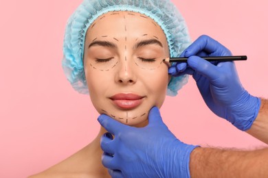 Photo of Doctor with pencil preparing patient for cosmetic surgery operation on pink background, closeup