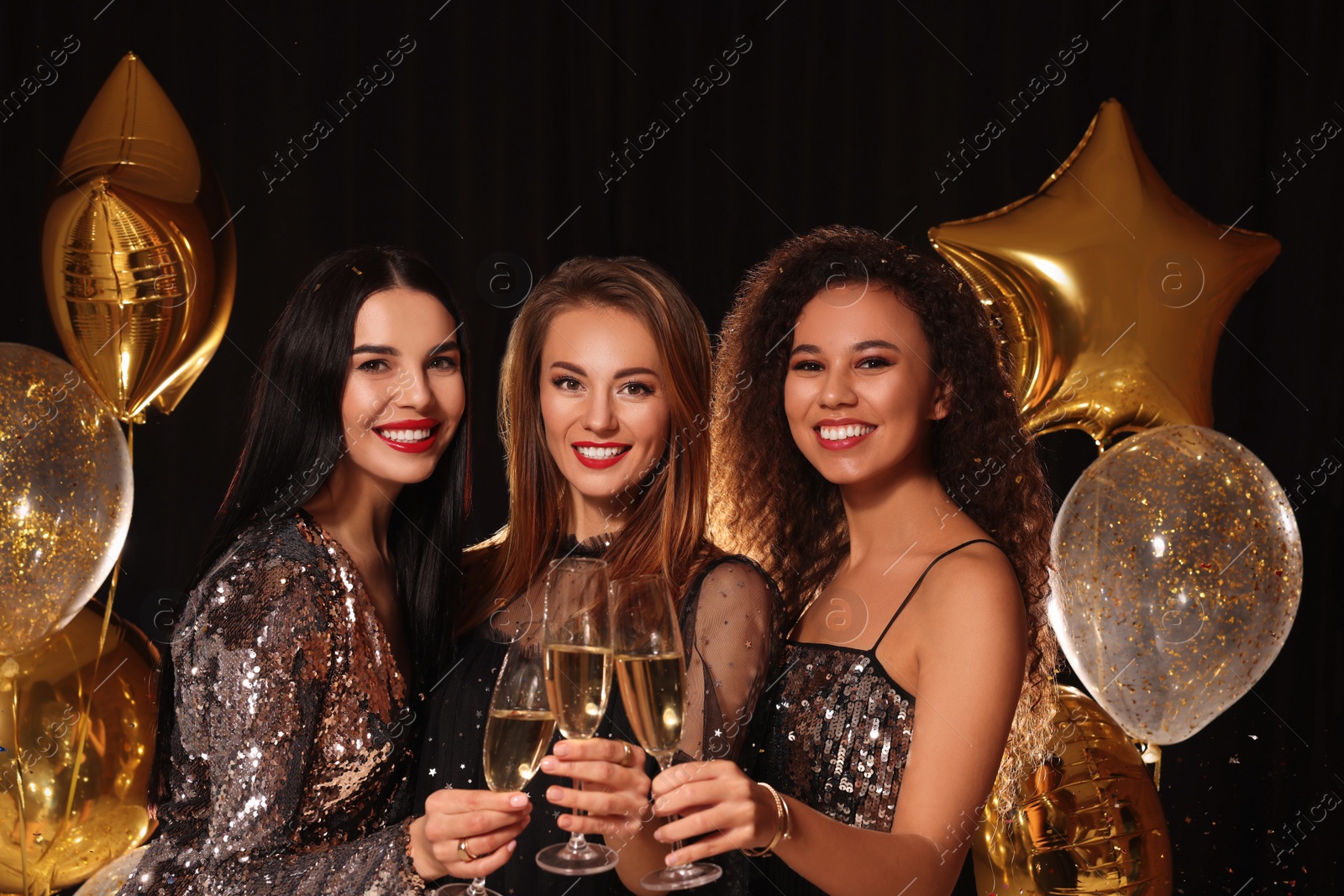 Photo of Happy women with glasses of sparkling wine celebrating New Year on black background