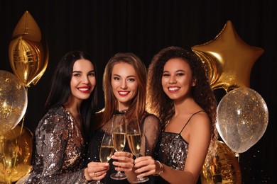 Photo of Happy women with glasses of sparkling wine celebrating New Year on black background