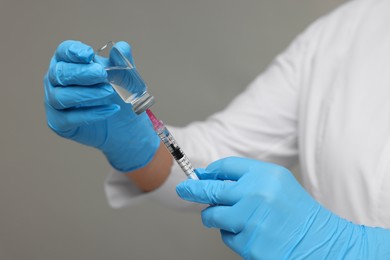 Doctor filling syringe with medication from glass vial on grey background, closeup