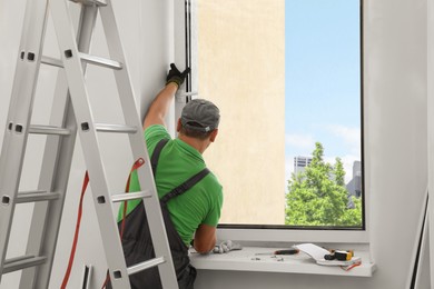 Photo of Worker in uniform installing double glazing window indoors, back view