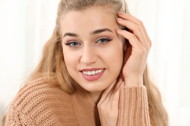 Portrait of attractive smiling young woman in cozy warm sweater on light background