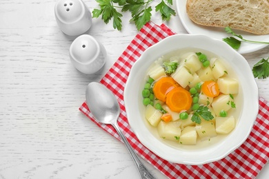 Photo of Bowl of fresh homemade vegetable soup served on white wooden table, flat lay. Space for text