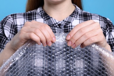 Photo of Woman popping bubble wrap on turquoise background, closeup. Stress relief