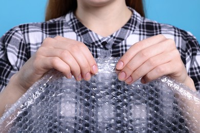 Woman popping bubble wrap on turquoise background, closeup. Stress relief