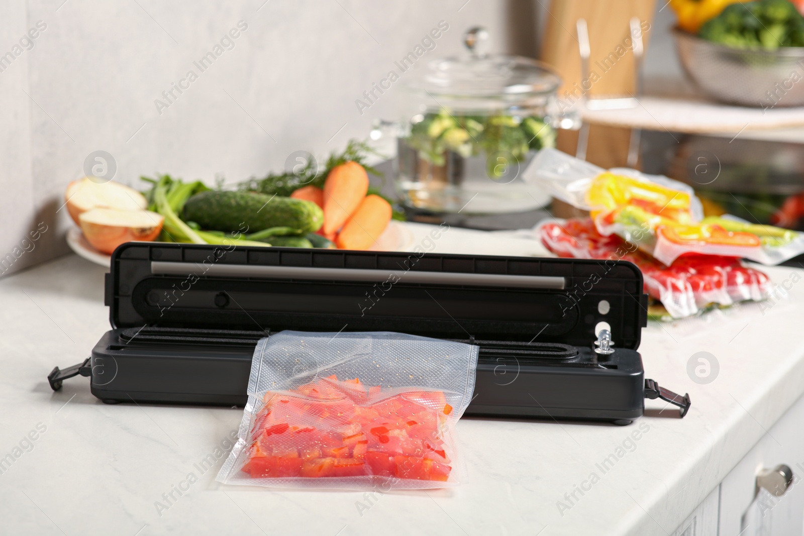 Photo of Sealer for vacuum packing with red pepper in plastic bag on white table indoors