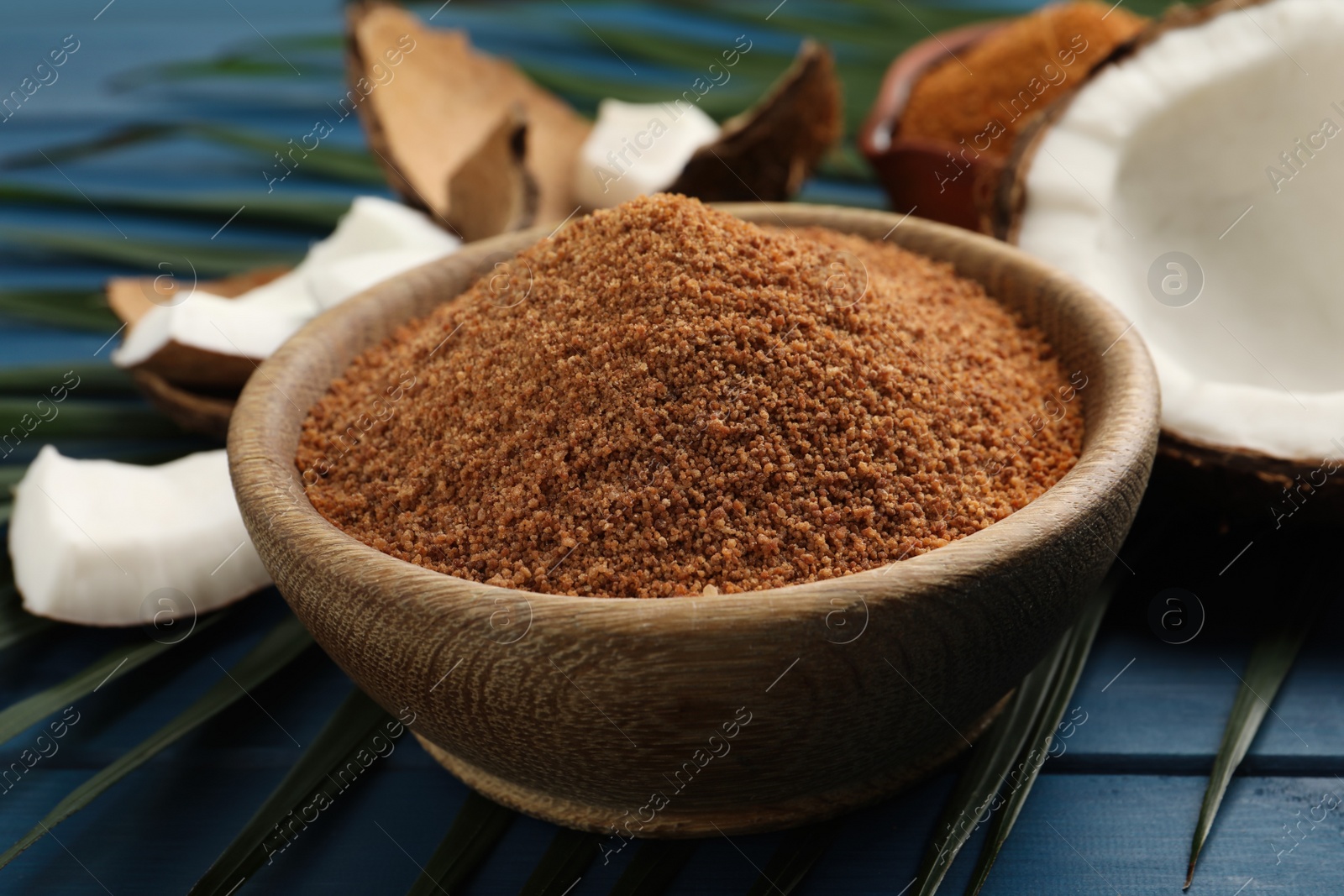 Photo of Natural coconut sugar in bowl on blue wooden table, closeup