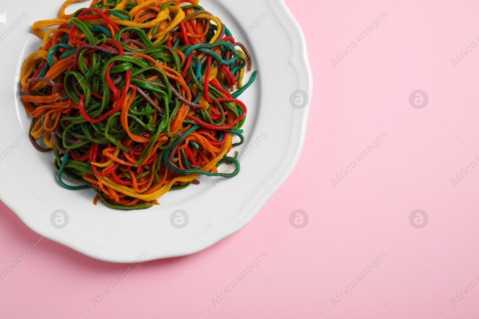 Photo of Plate of spaghetti painted with different food colorings on pink background, top view. Space for text