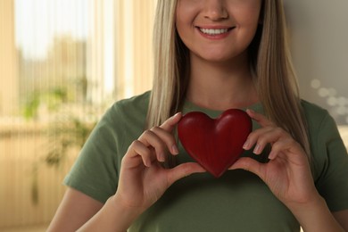 Happy volunteer holding red heart with hands indoors, closeup