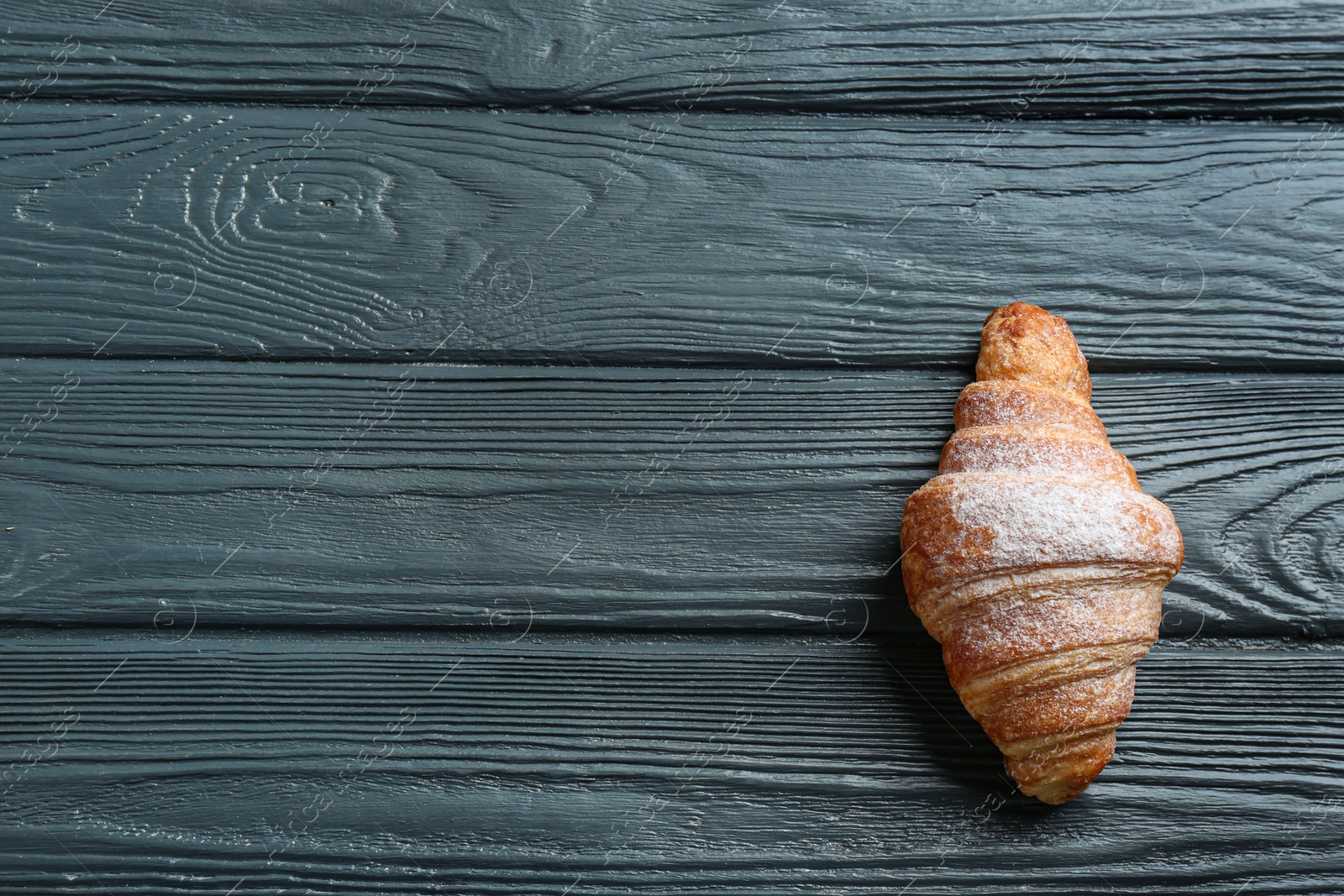 Photo of Tasty croissant with powdered sugar and space for text on dark wooden background, top view. French pastry