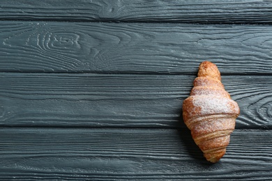 Photo of Tasty croissant with powdered sugar and space for text on dark wooden background, top view. French pastry