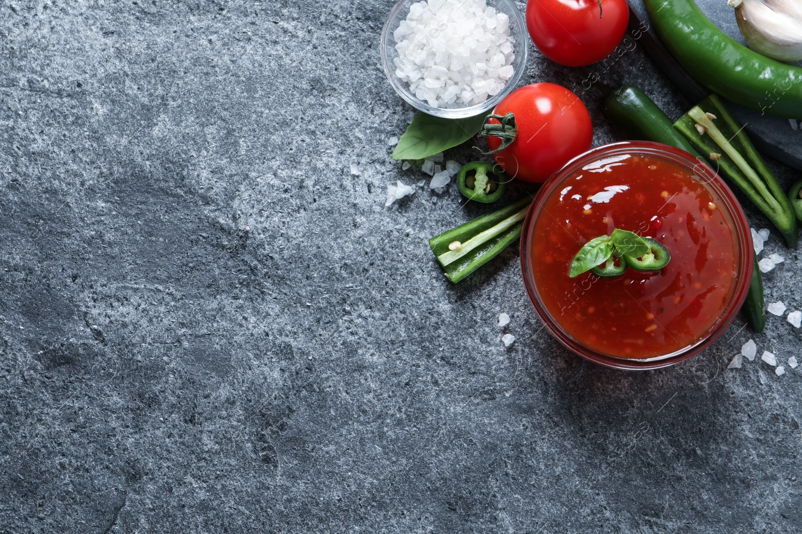 Photo of Spicy chili sauce and ingredients on grey table, flat lay. Space for text