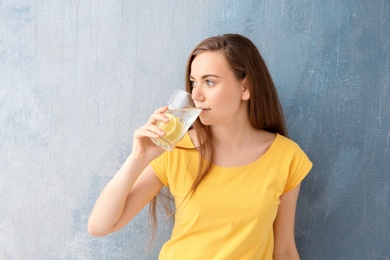 Young woman drinking lemon water on color background