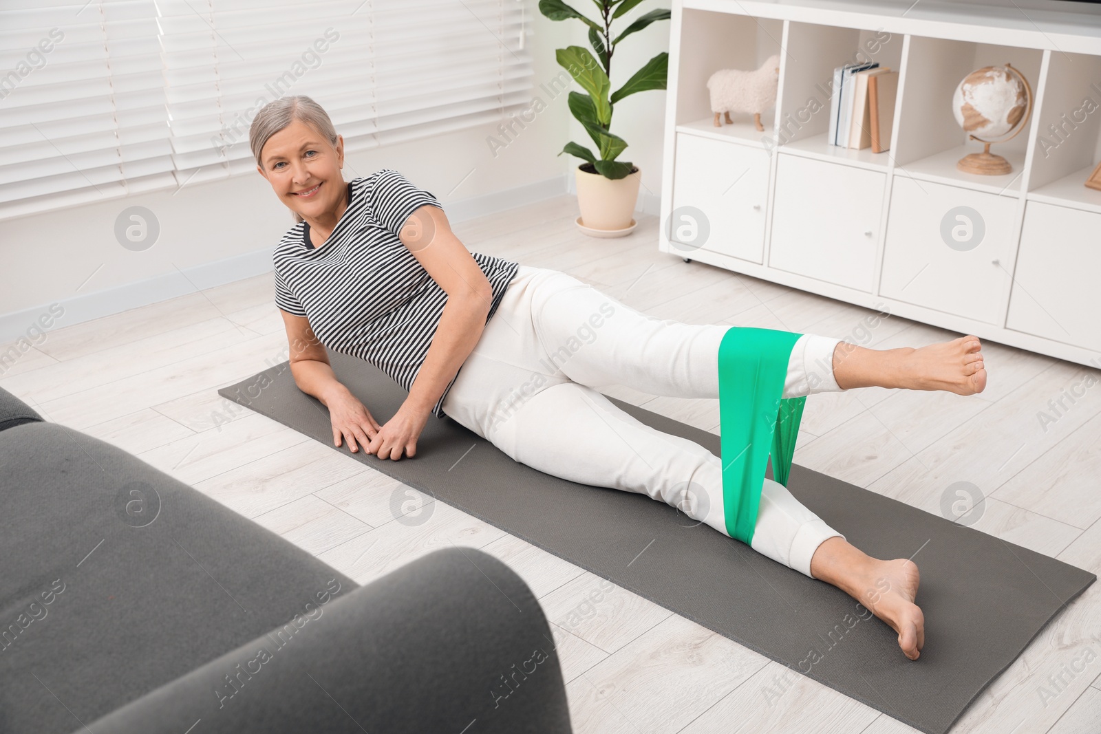 Photo of Senior woman doing exercise with fitness elastic band on mat at home