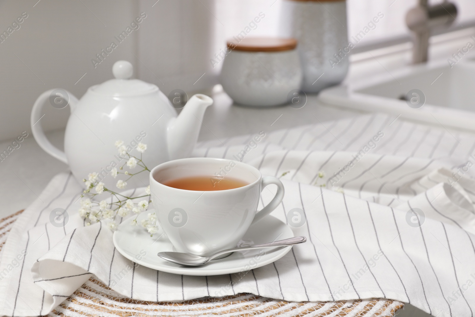 Photo of White teapot with saucer and cup of tea on countertop in kitchen