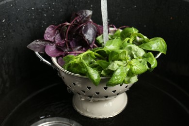 Photo of Washing different fresh basil leaves under tap water in metal colander in sink