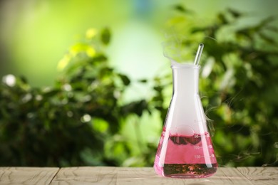 Laboratory flask with colorful liquid on wooden table outdoors, space for text. Chemical reaction