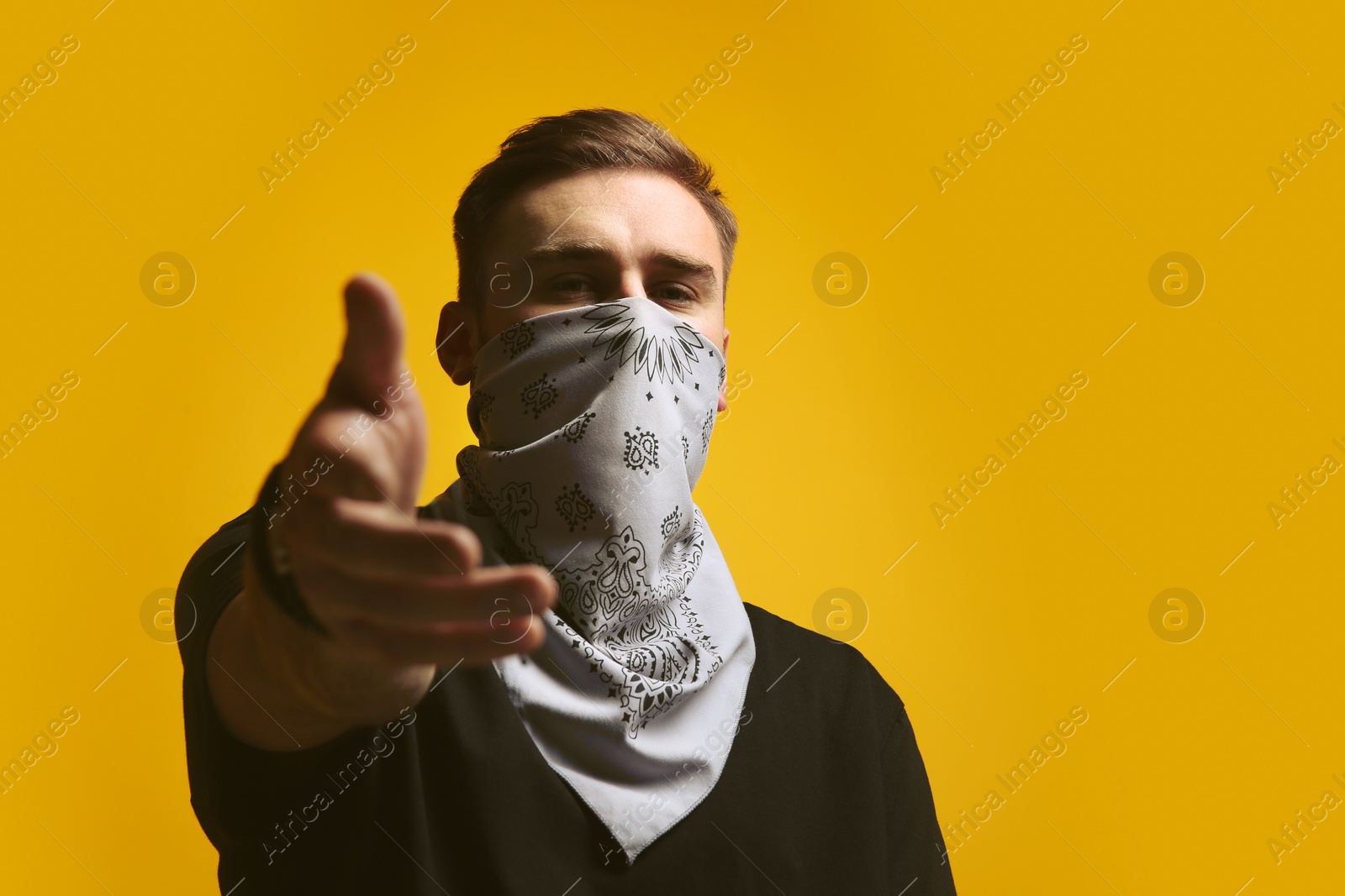 Photo of Young man with bandana covering his face on yellow background, space for text