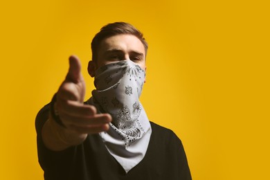 Photo of Young man with bandana covering his face on yellow background, space for text