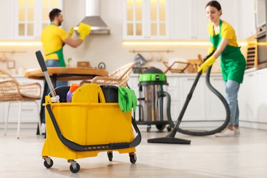 Photo of Professional janitors working in kitchen, focus on bucket with equipment