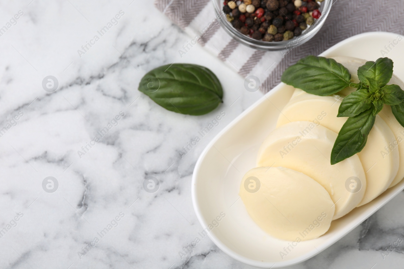 Photo of Plate with tasty mozzarella slices and basil leaves on white marble table, above view. Space for text