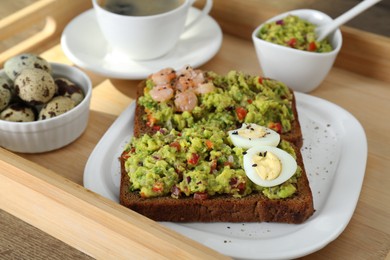 Slices of bread with tasty guacamole, eggs, shrimp and coffee on wooden table, closeup