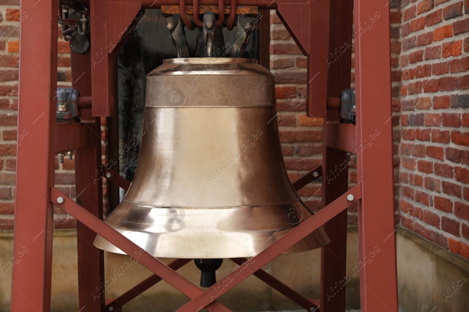 Photo of Wooden construction with large old bronze bell near brick wall outdoors