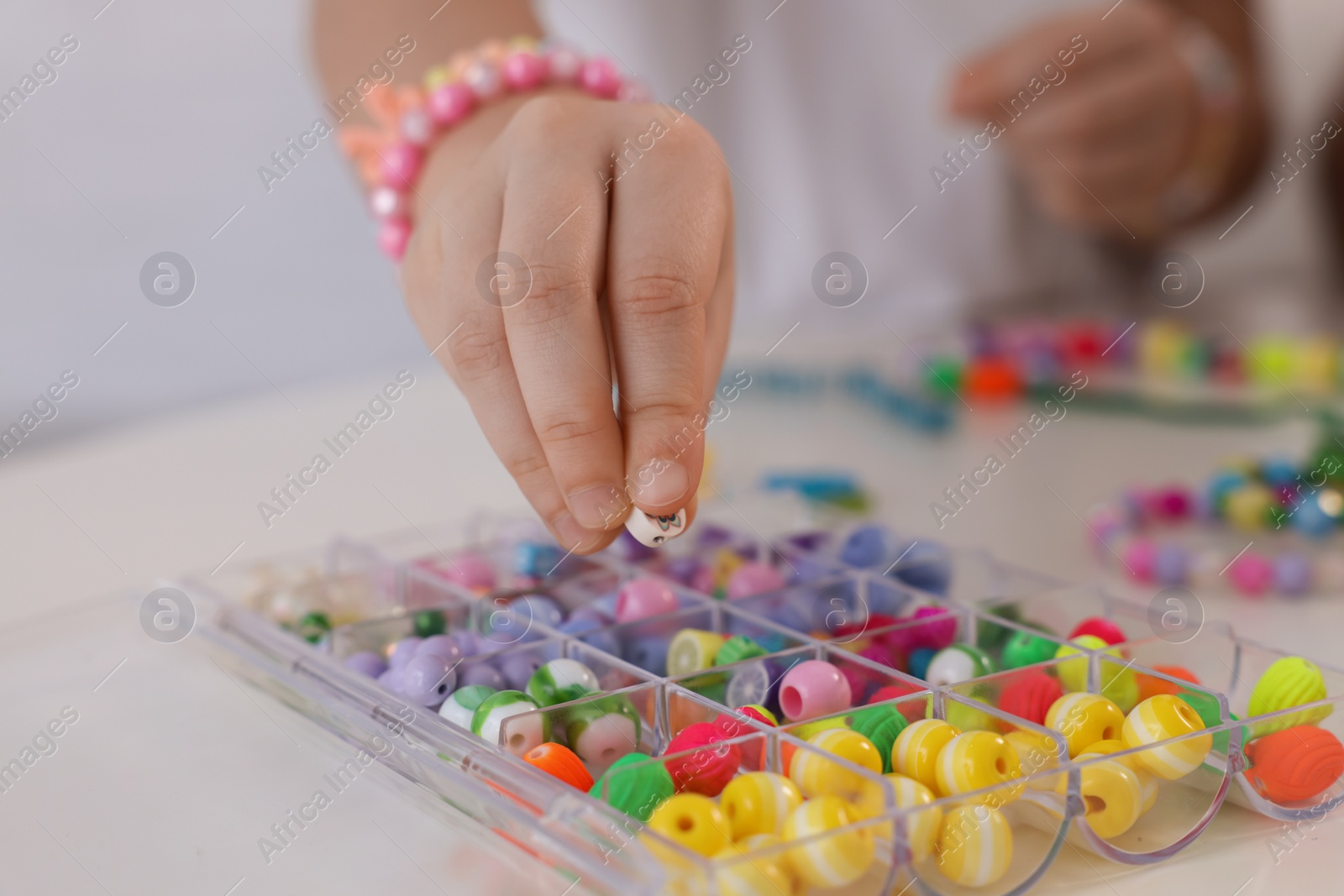 Photo of Little girl making beaded jewelry at table, closeup